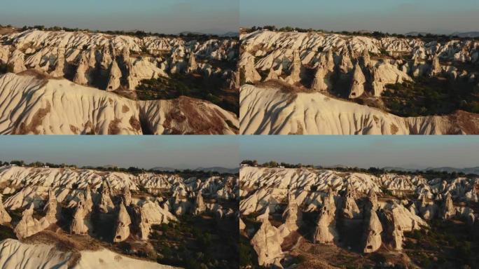 在夏季日落时，无人驾驶飞机在土耳其卡帕多西亚的大气风景中与美丽的高大白色岩石一起平移。