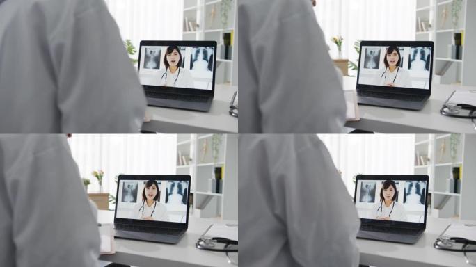 年轻的亚洲女士医生穿着白色医疗制服，使用笔记本电脑与健康诊所服务台的高级医生交谈视频电话会议。