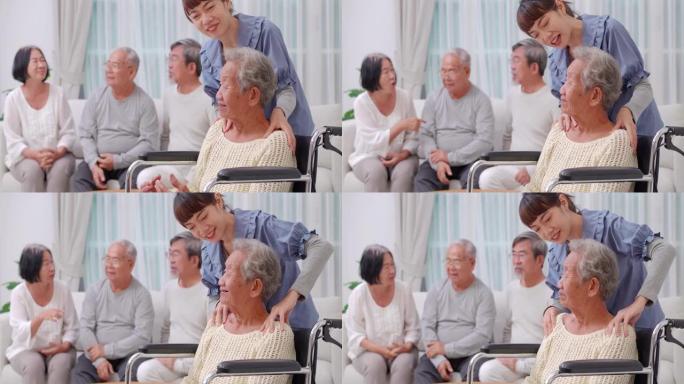 在疗养院，亚洲老年妇女坐在轮椅上，与亚洲年轻女性家庭护理人员交谈，同时按摩亚洲祖母的肩膀，护士在养老