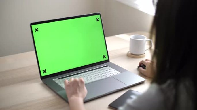 亚洲妇女在家中使用带有绿屏的笔记本电脑