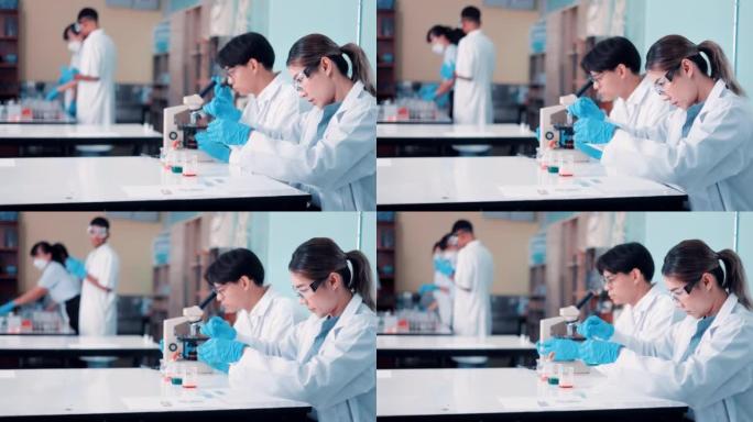 在研究实验室中，穿着白大褂的工业科学家和工程师组成的多元化团队与显微镜一起工作