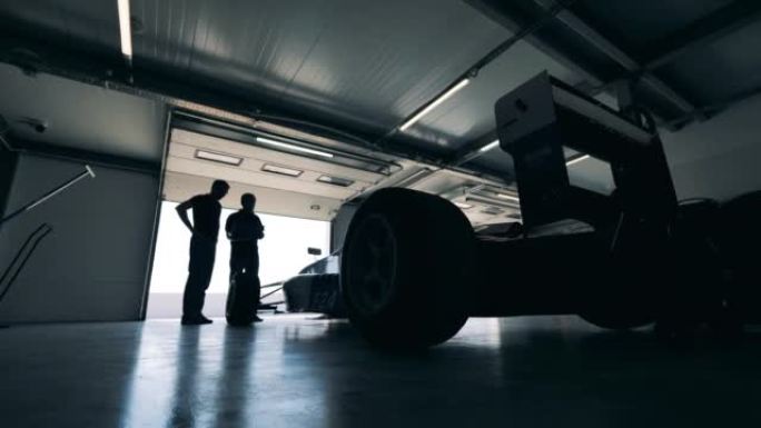 两名赛车手正在车库里观察跑车