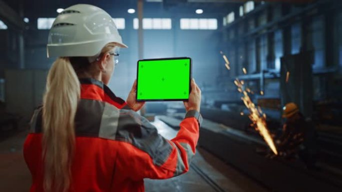 专业的重工业工程师使用带有绿屏模拟显示的平板电脑。在金属制造仓库工作的女性工业专家，背景是火花。