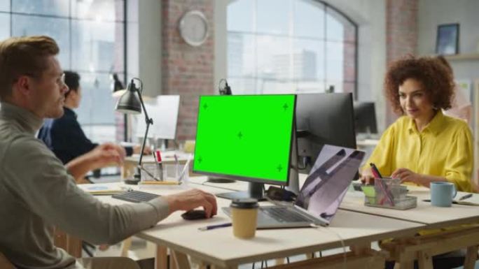 在现代明亮的办公室里，多民族的富有创造力的同事在计算机上工作。男性管理员使用绿屏准备演示文稿。混血儿