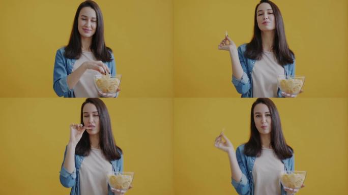 快乐女人吃薯片的肖像在黄色背景上愉快地微笑