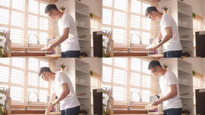 快乐年轻的亚洲人洗碗，同时在厨房打扫房子。