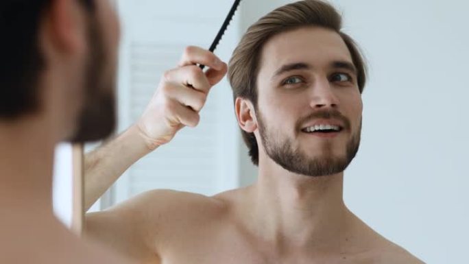 快乐英俊的男人用梳子梳着发型，看着镜子。