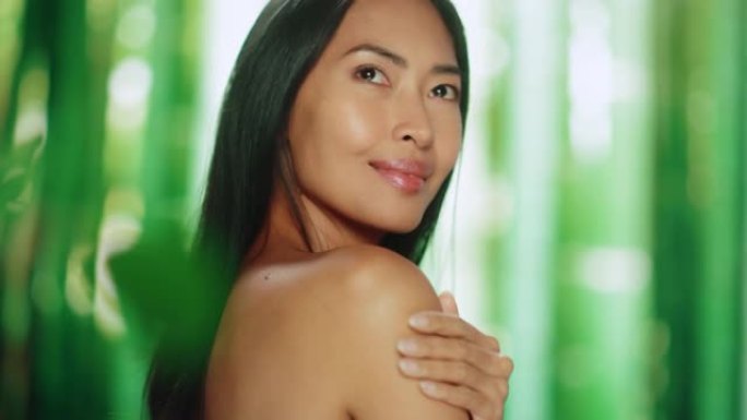 美丽的亚洲女人抚摸着她完美柔软的肩膀，脖子，性感地微笑。享受她美丽的女性。有机化妆品护肤品。天然绿色