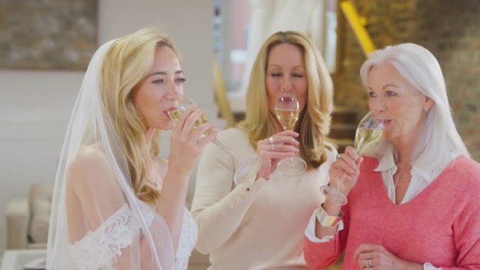 祖母与母亲和成年女儿一起用香槟庆祝，孙女在新娘商店选择并试穿婚纱-慢动作拍摄