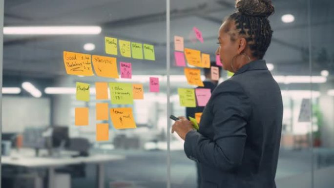 非裔美国女商人用纸质笔记在办公室墙上创建项目计划。时尚自信的经理，从事商业、金融和营销项目。多元化团
