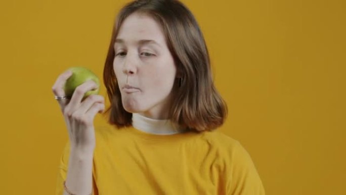 吃苹果的年轻女子在黄色背景上微笑的慢动作肖像