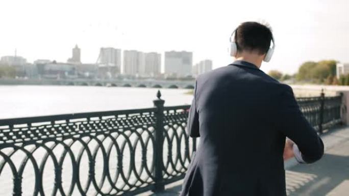 快乐的人走在河堤上戴着耳机跳舞，看着智能手机屏幕