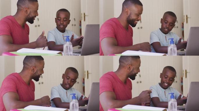 非裔美国人的父亲在坐着笔记本电脑和消毒瓶时帮助儿子做作业
