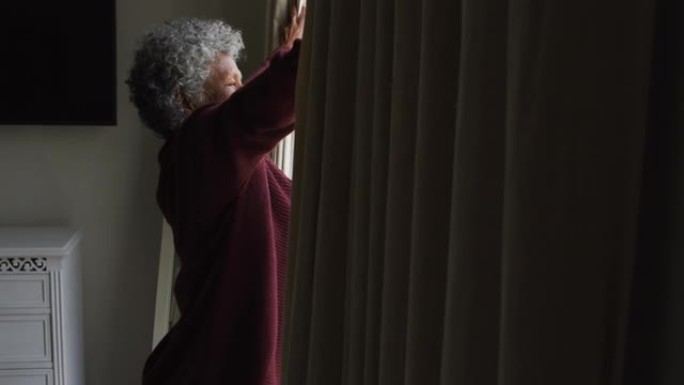 资深非裔美国妇女在家中打开窗户的窗帘