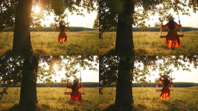 慢动作，手持镜头，一名穿着红色连衣裙的年轻成年女性摇摆，坐在悬挂在阳光充足的草地上的大树枝上的绳索秋