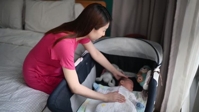 亚洲华裔年轻母亲在卧室的婴儿床中轻拍婴儿男婴