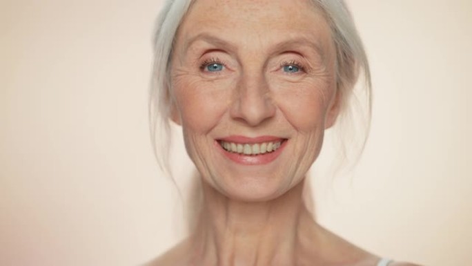 看着镜头，微笑着的高级女性的肖像。有着天然灰色头发、蓝色眼睛的老年女士。优雅的老年概念，用于护肤，美