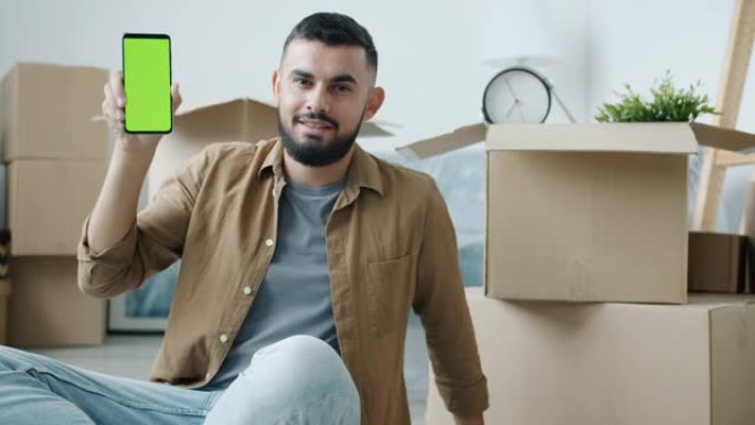 在新公寓中拿着带有绿色色度键屏幕的智能手机的中东男子肖像
