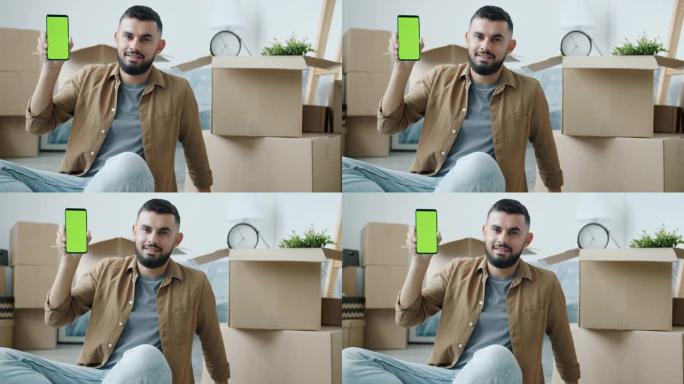 在新公寓中拿着带有绿色色度键屏幕的智能手机的中东男子肖像