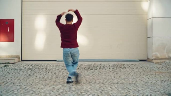 在城市老城区的街道上散步时，开朗快乐的成年男子穿着便服积极跳舞。在车库门前的城市环境中拍摄的场景。侧