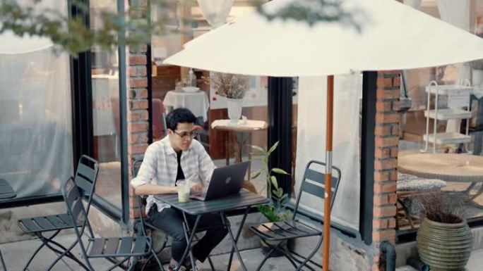 年轻的亚洲男子使用现代技术在人行道咖啡馆进行远程视频连接