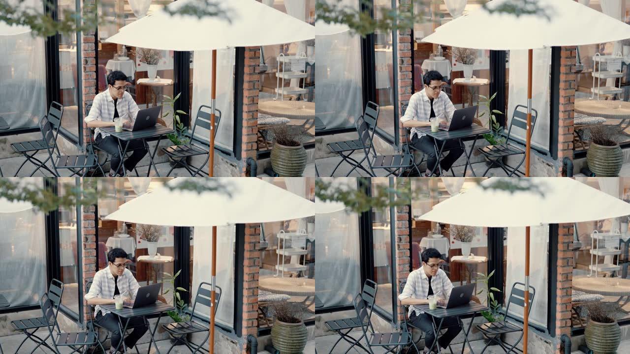 年轻的亚洲男子使用现代技术在人行道咖啡馆进行远程视频连接