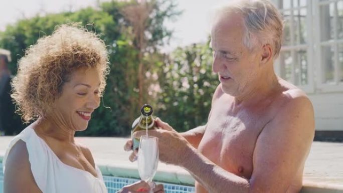 退休的高级夫妇暑假在游泳池里放松，庆祝开香槟