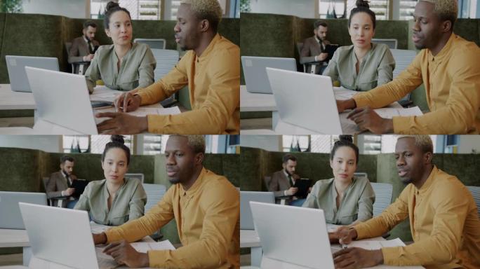 非裔美国员工使用笔记本电脑并在开放空间办公室与女同事交谈