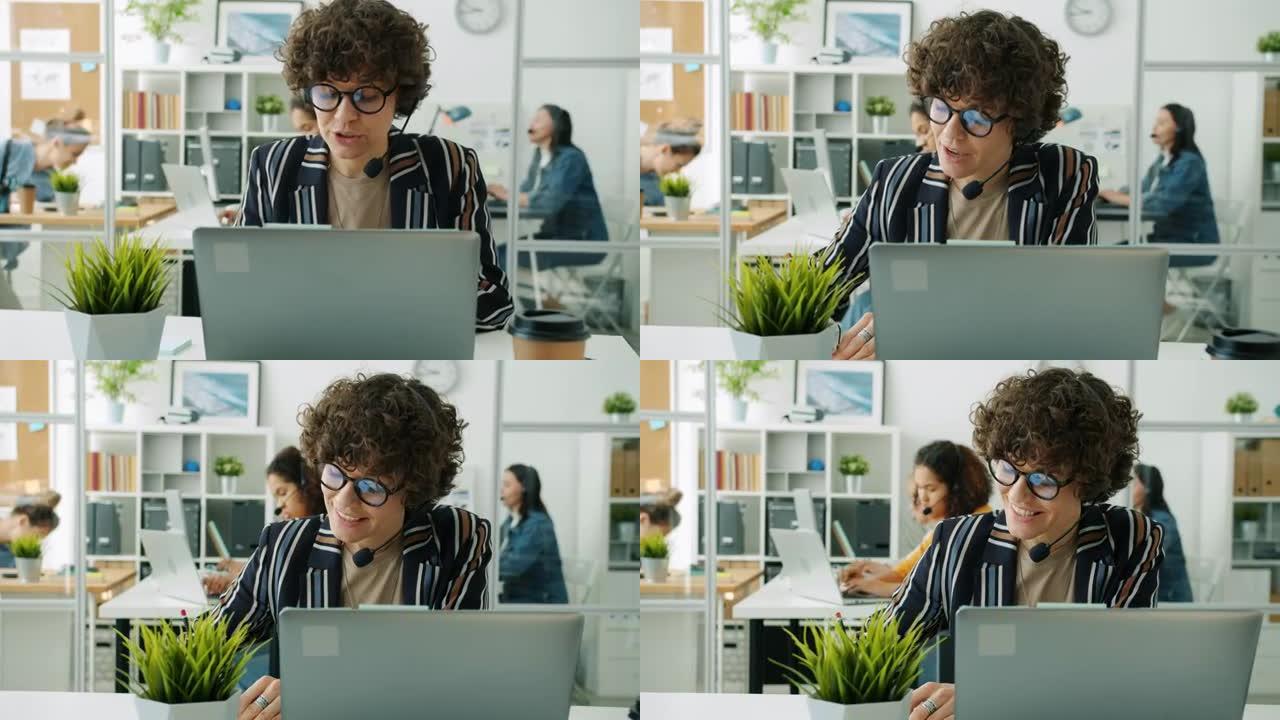 有吸引力的女士呼叫中心工作人员在工作场所用笔记本电脑打电话和打字的肖像