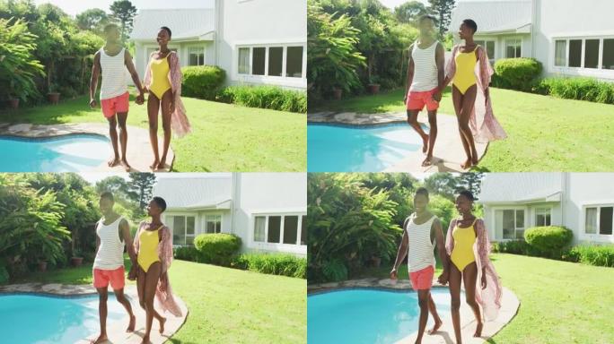 快乐的非洲裔美国夫妇在阳光明媚的花园里牵着手走在游泳池边微笑