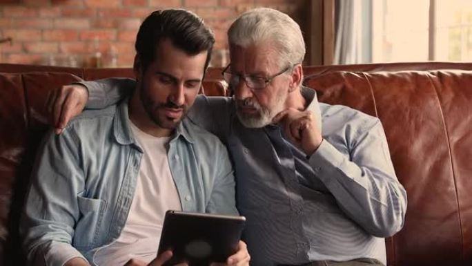 微笑的男人在平板电脑上向老爸展示有趣的照片。