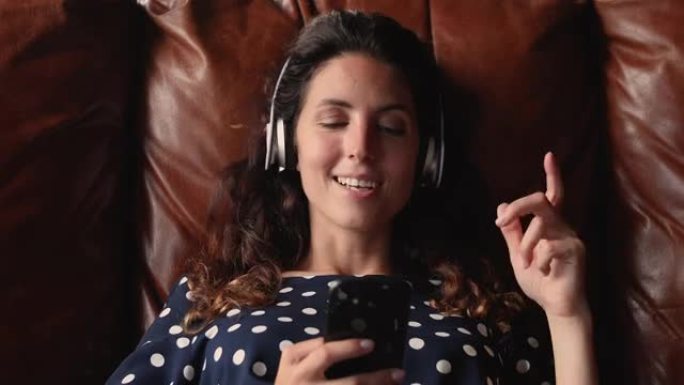 女人躺在沙发上拿着智能手机通过耳机听音乐