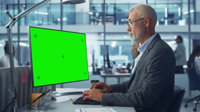 多样化的现代办公室: 高级高加索信息技术人员使用带有绿色色度键屏幕的台式计算机。工程师管理员从事电子
