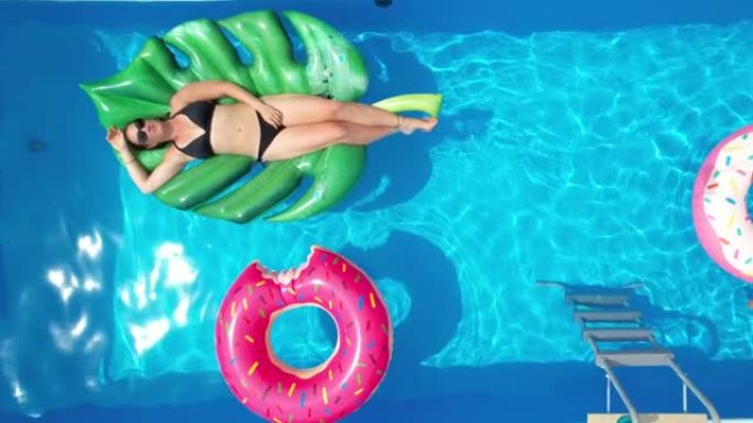 垂直: 无忧无虑的女人在蓝色的花园游泳池里享受阳光明媚的夏日。