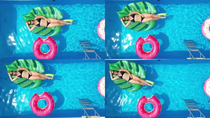 垂直: 无忧无虑的女人在蓝色的花园游泳池里享受阳光明媚的夏日。