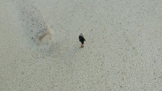 气候变化。由于气候变化和全球变暖造成的干旱，一个饱受摧残的农民走过干旱大坝的图案化的破裂泥面的特写鸟