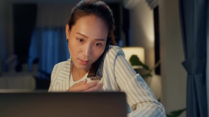 年轻快乐的亚洲女商人穿着正式的坐在办公桌前，用笔记本电脑和平板电脑打字，晚上在家舒适的客厅打电话给同