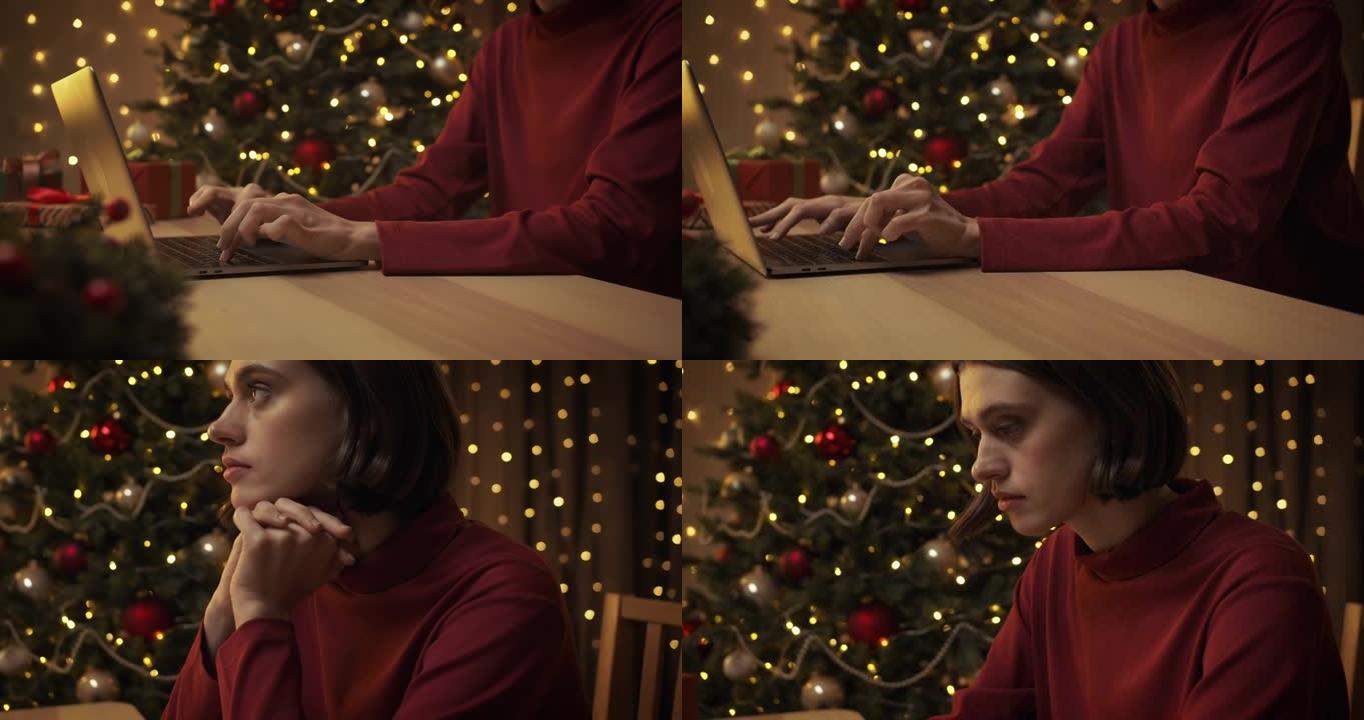 一位穿着红色毛衣的年轻美女正坐在带圣诞灯的厨房的桌子旁，在笔记本电脑上打字。