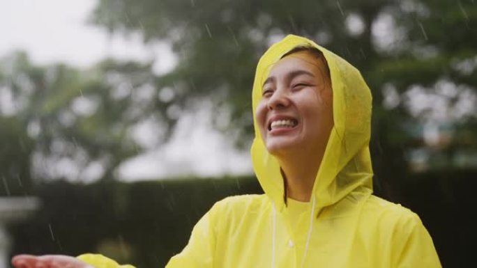 穿着黄色雨衣的亚洲女人暴露在雨中，慢动作，在户外享受淋浴
