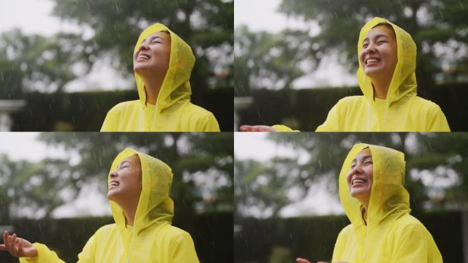 穿着黄色雨衣的亚洲女人暴露在雨中，慢动作，在户外享受淋浴