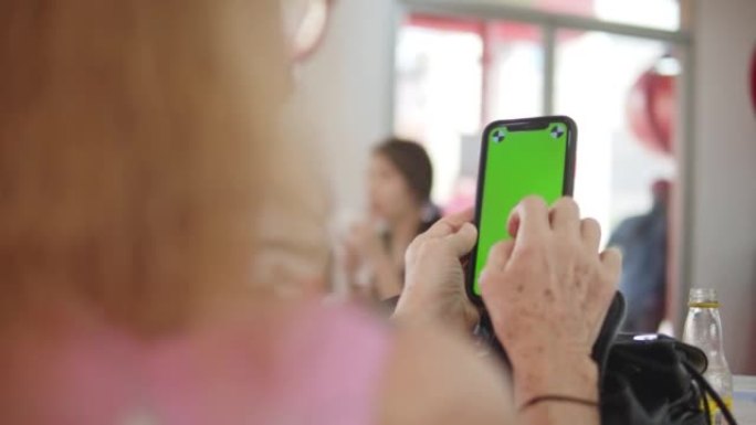 高级女性在咖啡馆使用带有绿屏的智能手机，跟踪镜头