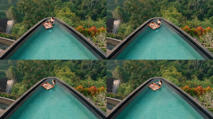 俯视图女人在游泳池吃早餐，在豪华酒店水疗中心享受异国美食，可以看到热带丛林
