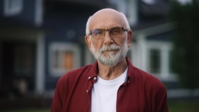 近距离拍摄一位戴着眼镜的开朗的老人的肖像，他戴着眼镜站在居民区房屋前的户外。退休的成年男子看着相机微