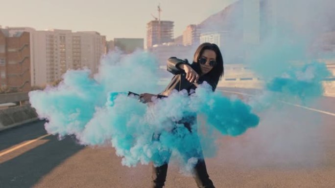 女孩在城市街头与蓝色烟雾手榴弹跳舞年轻女子嘻哈舞者用舞蹈慢动作庆祝创意表达