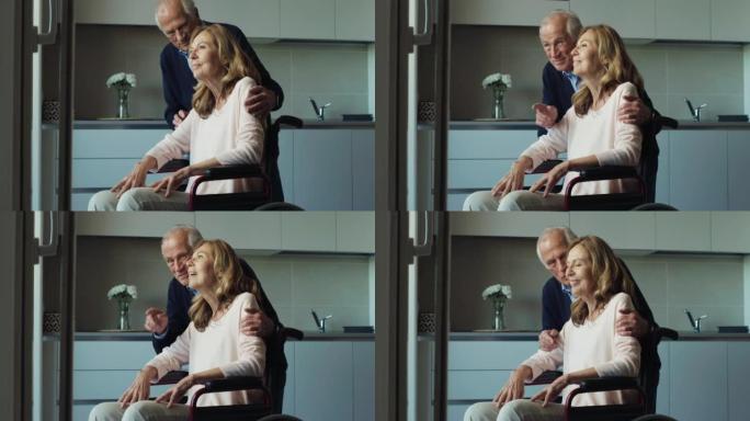 微笑的成熟丈夫拥抱轮椅上的残疾妻子的电影镜头，是在家中透过窗户看时永远永恒的爱的标志。生活观念，家庭