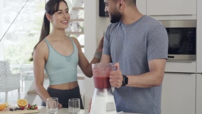健康健康的男人在家里的厨房里为他和他美丽的年轻女友制作运动饮料或冰沙。运动情侣在锻炼或锻炼前喝健康奶