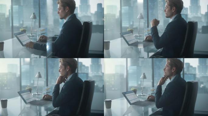 自信的商人穿着西装，坐在现代办公室的办公桌前，使用笔记本电脑，在窗户旁边，可以看到摩天大楼。成功的财
