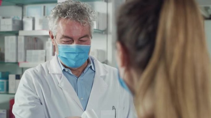 电影镜头，男药剂师带着医用口罩，用红外测温枪对着女病人测体温。新冠肺炎概念、防护、病毒传播、安全。