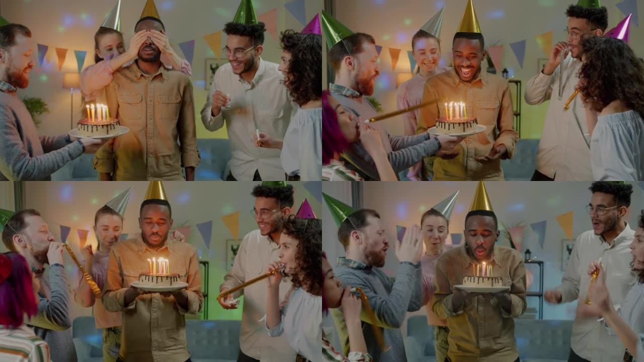惊讶的非洲裔美国男子在生日蛋糕上吹蜡烛，而朋友在家庭聚会上笑着拍手