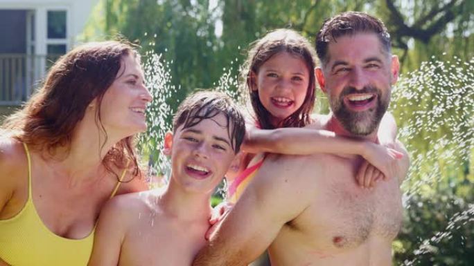 穿着游泳衣的家庭肖像在花园洒水车的水中玩耍